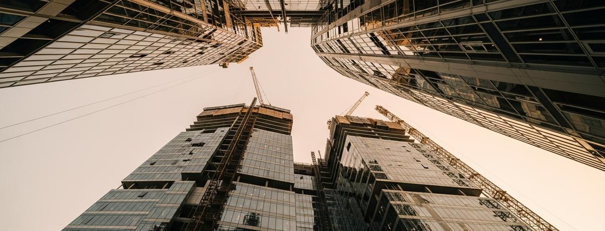  Edificio moderno de vidrio y acero fotografiado desde ángulo bajo con grúas de construcción visible, simbolizando el crecimiento continuo y el potencial ilimitado de una práctica profesional sin restricciones.